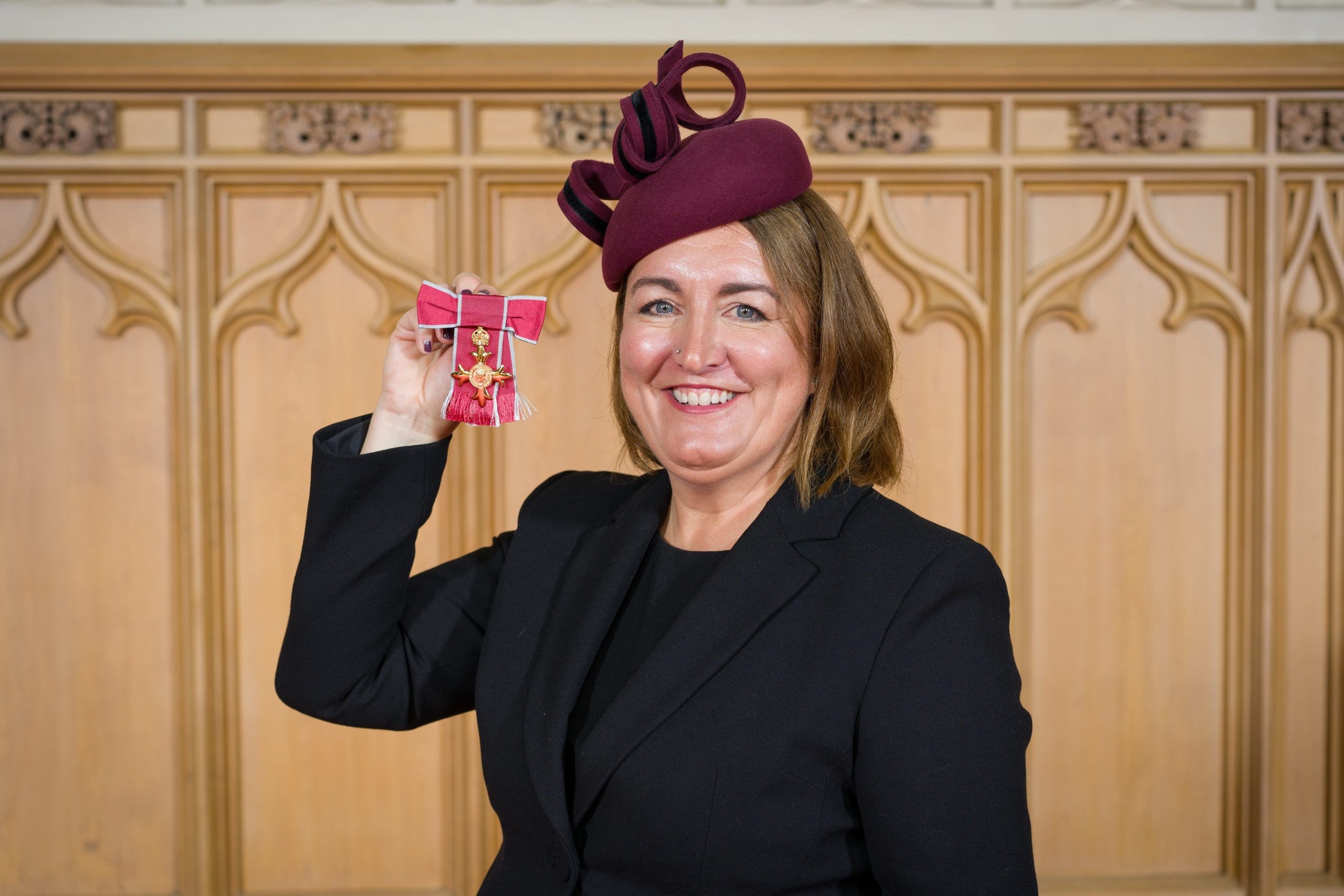A picture of Kate Davies after receiving her OBE. Kate is smiling and holding the award to the camera.
